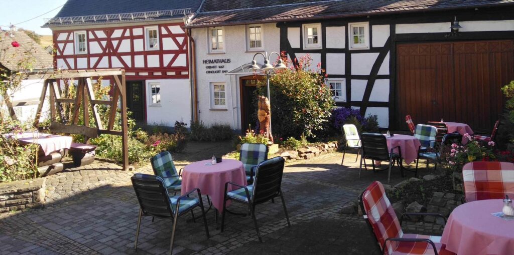 Gemütlicher Innenhof des Dorfcafés Daubach mit Fachwerkhaus, gedeckten Tischen und Gartenambiente – beliebter Treffpunkt für Wanderer an Sonn- und Feiertagen.